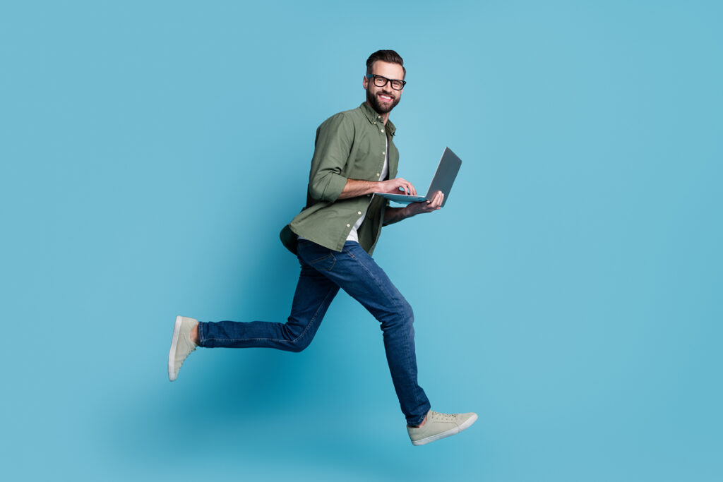 A man smiles while running with a laptop in his hands