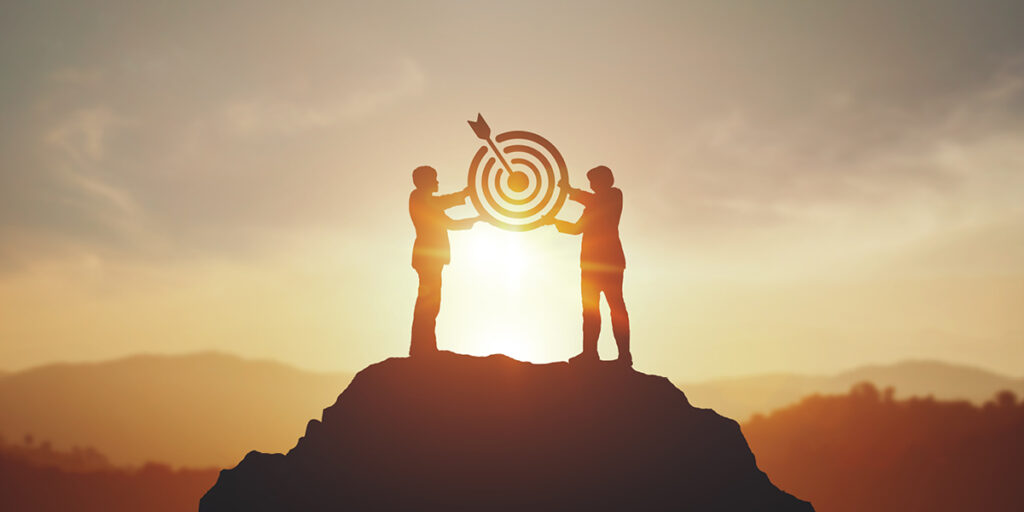 Two people holding a target at the top of a mountain